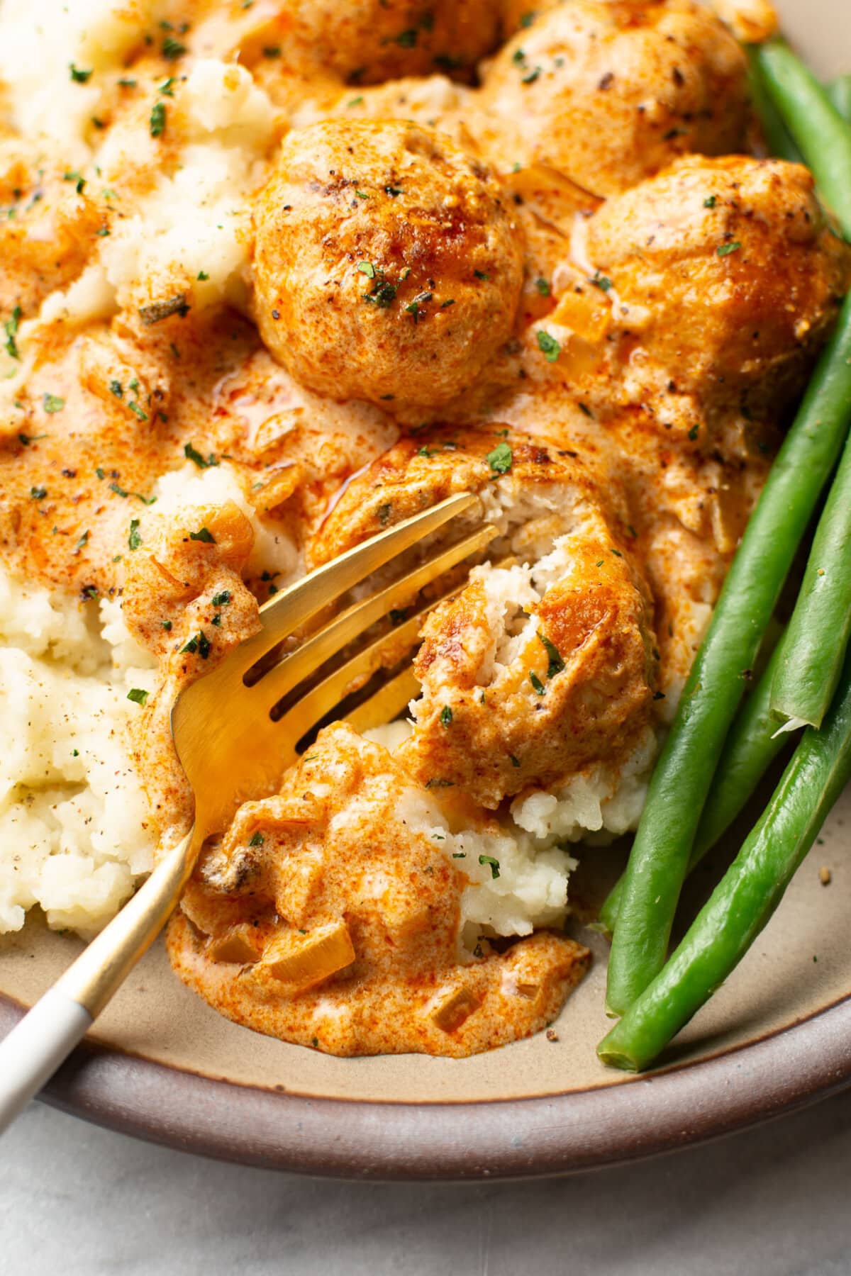 a plate with paprika chicken meatballs, mashed potatoes, and green beans