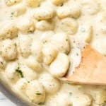 a skillet with creamy alfredo gnocchi and a wooden spoon