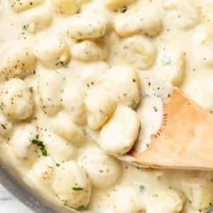 a skillet with creamy alfredo gnocchi and a wooden spoon