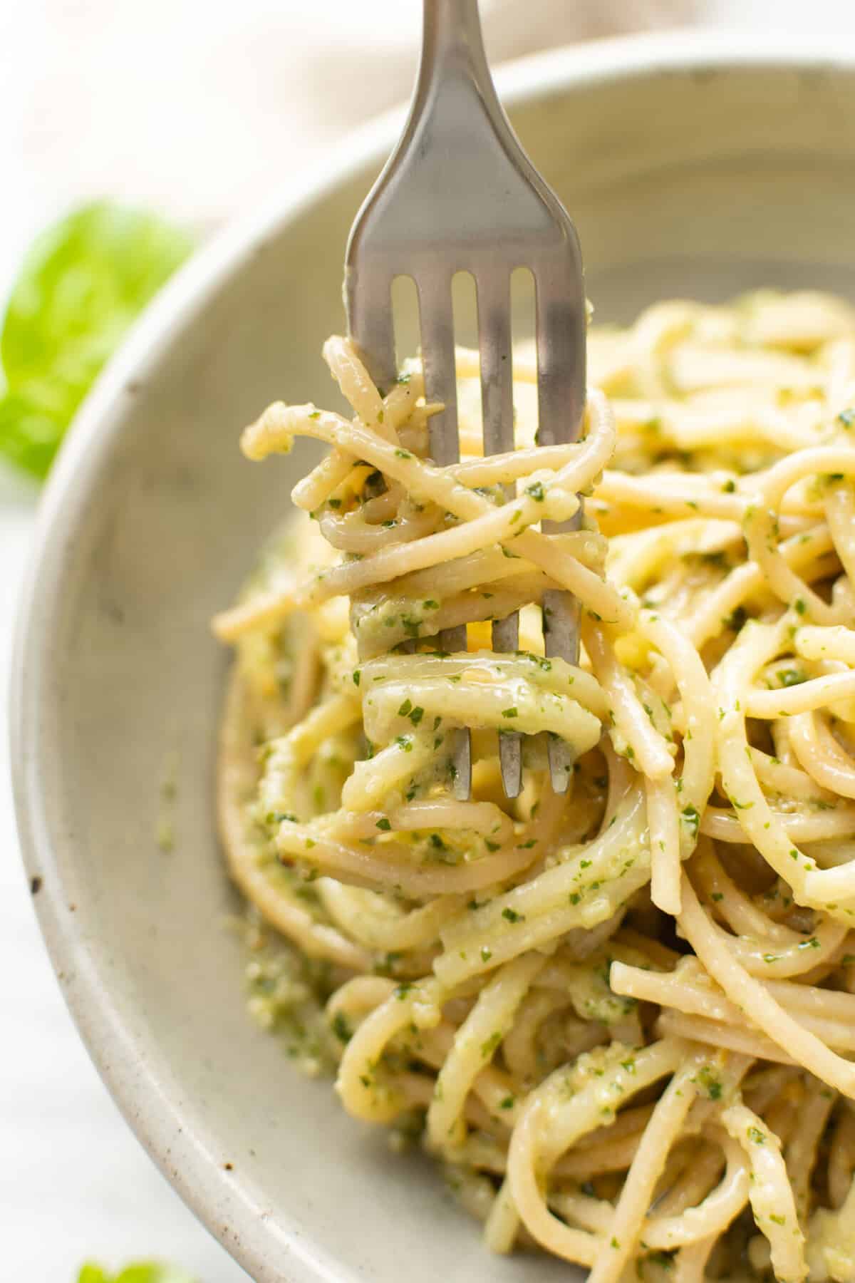 a bowl of spaghetti with pesto sauce and a fork