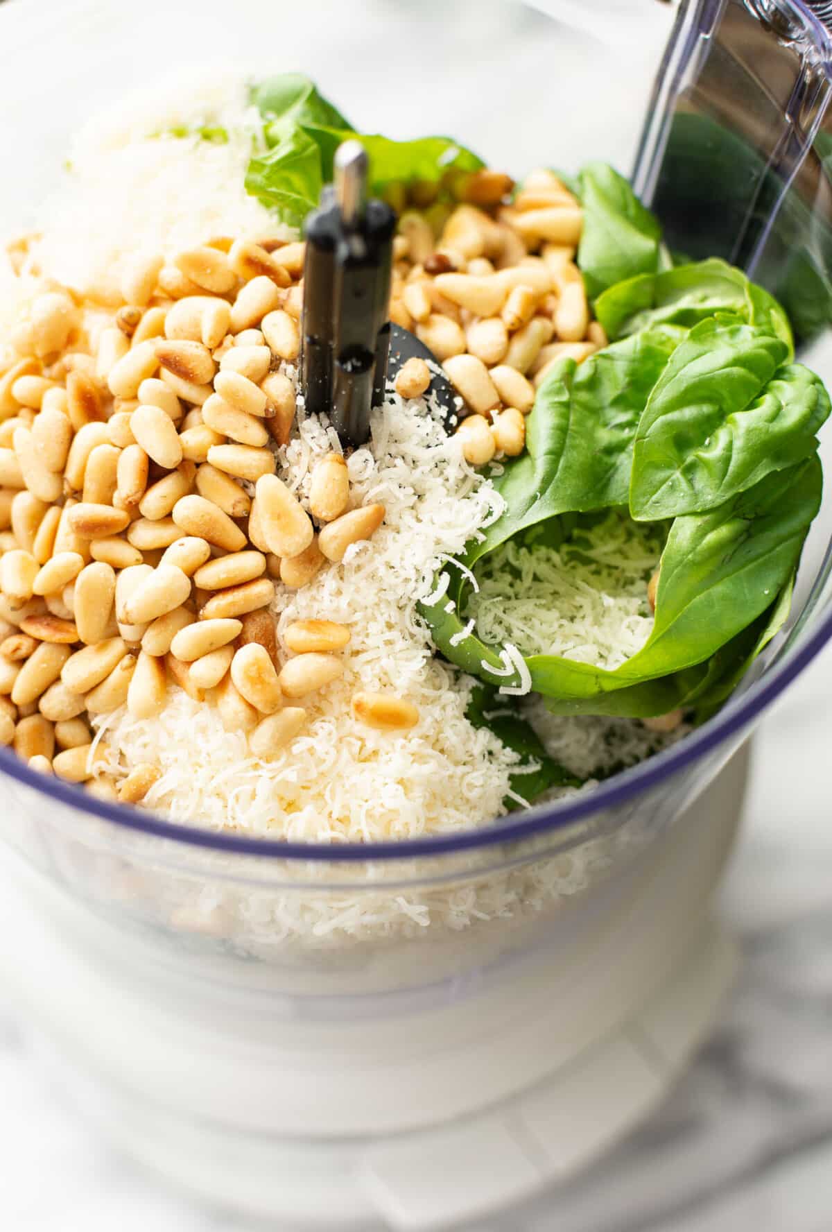 a food processor with ingredients for pesto