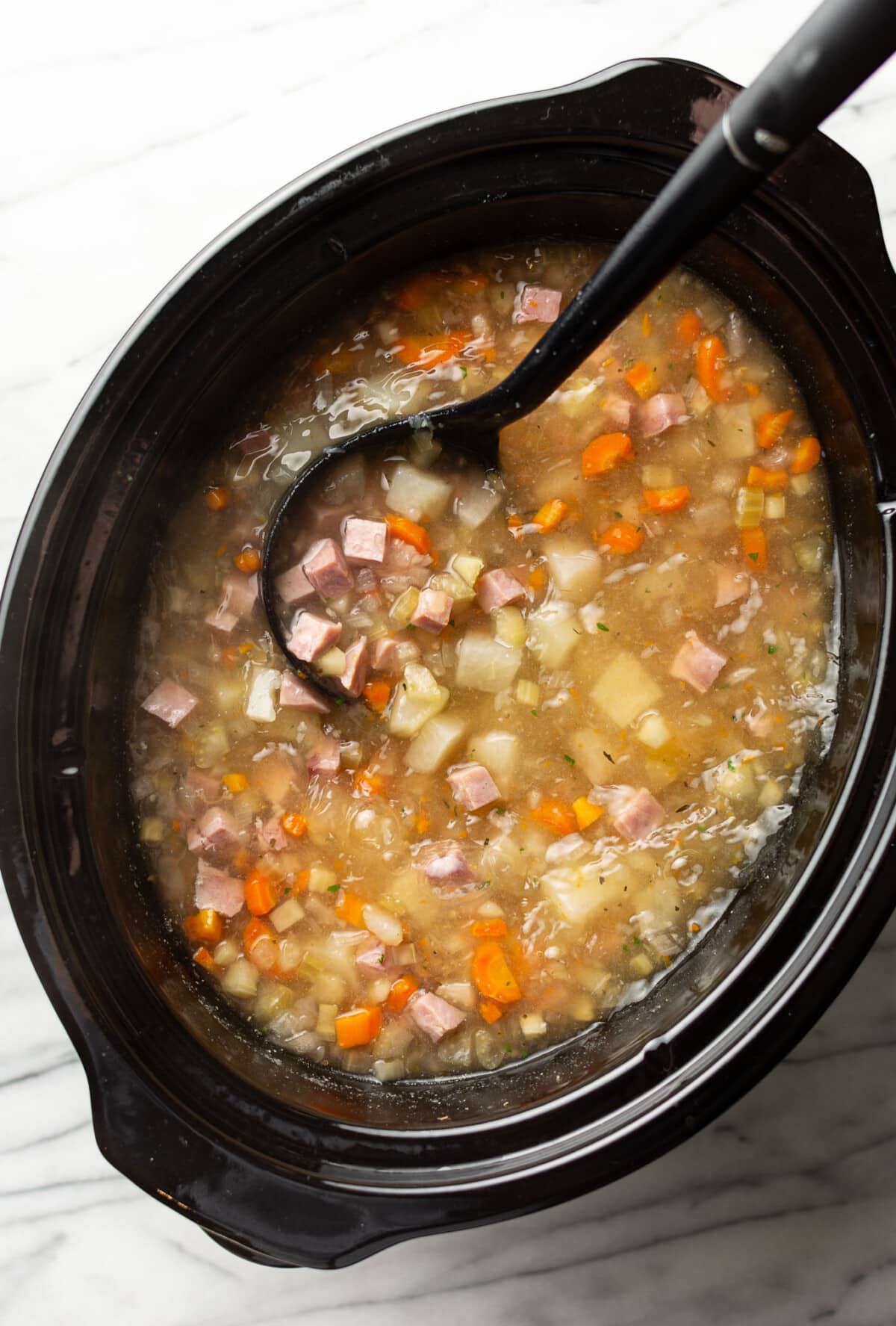 a slow cooker with ham and potato soup and a ladle