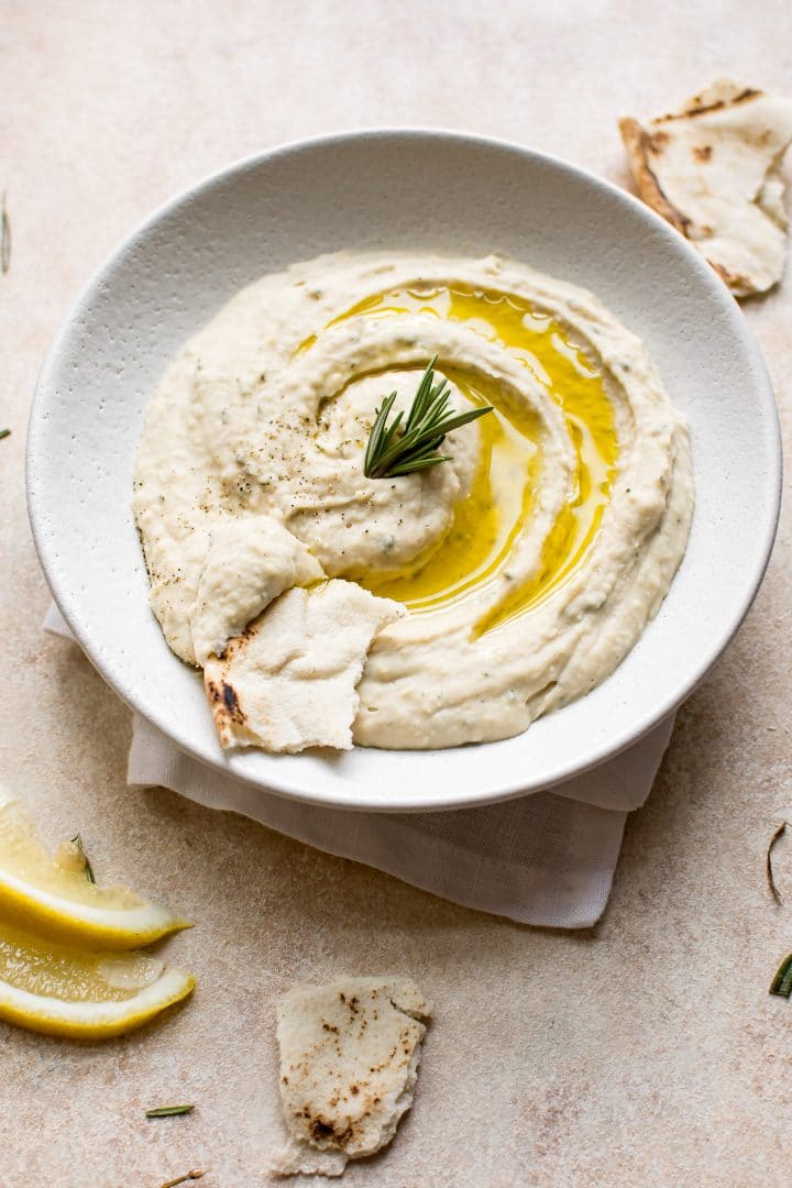 vegan white bean rosemary dip in a bowl with a sprig of rosemary and pita bread