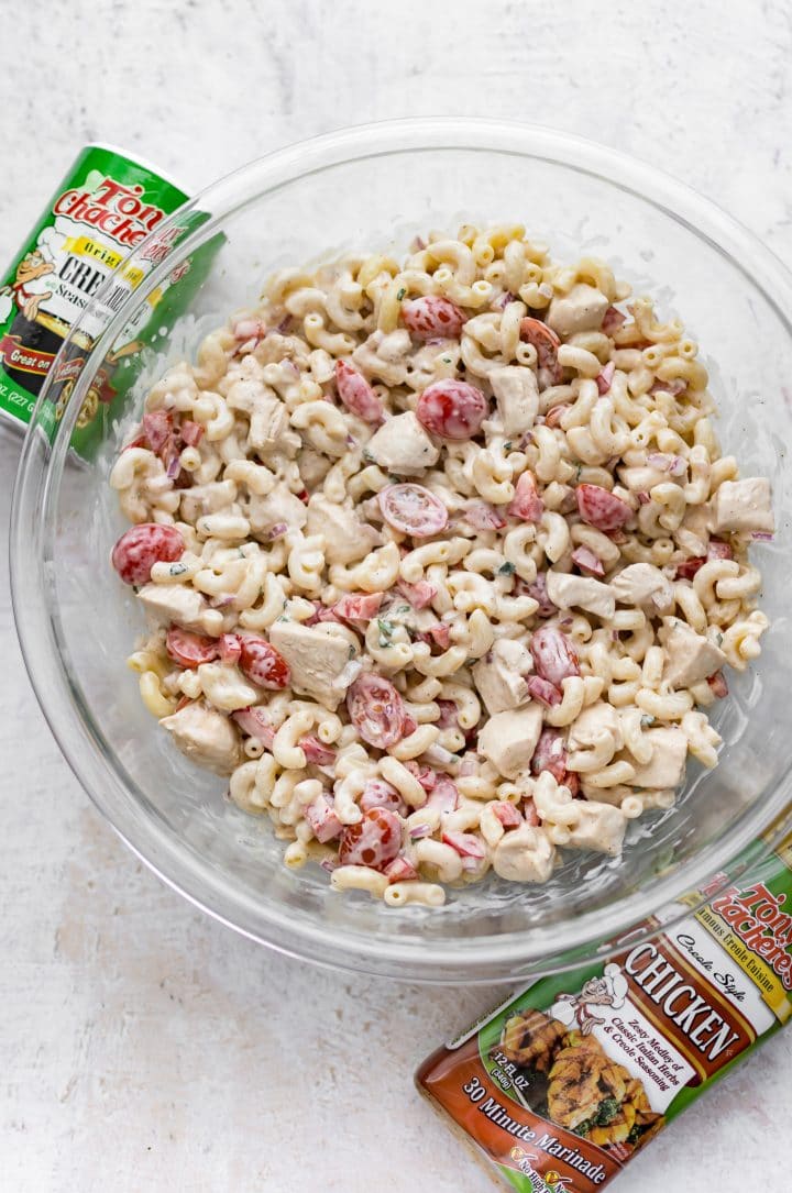 glass serving bowl with cajun pasta salad with chicken and little tomatoes beside tony chachere's products