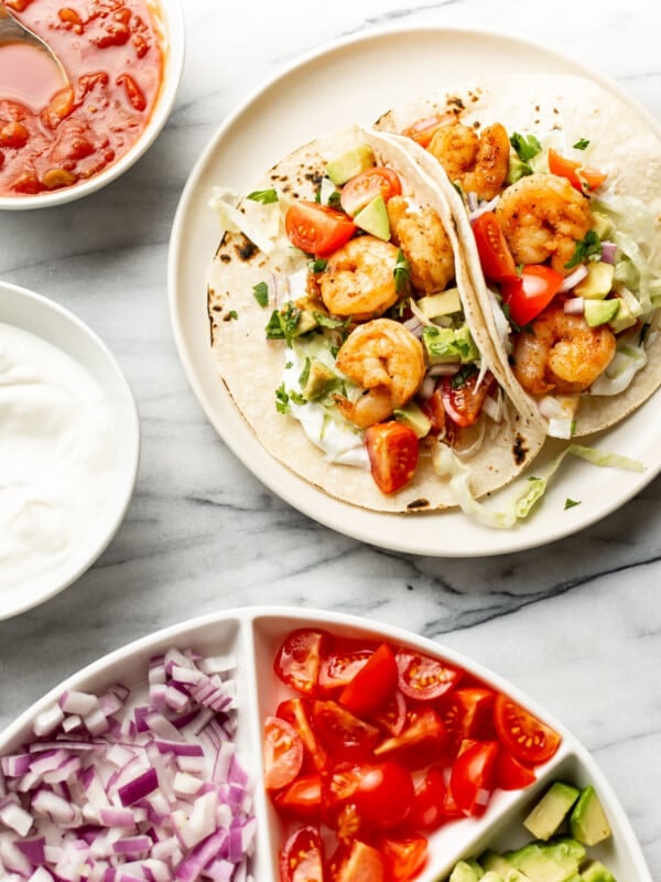 a plate with shrimp tacos next to fresh toppings