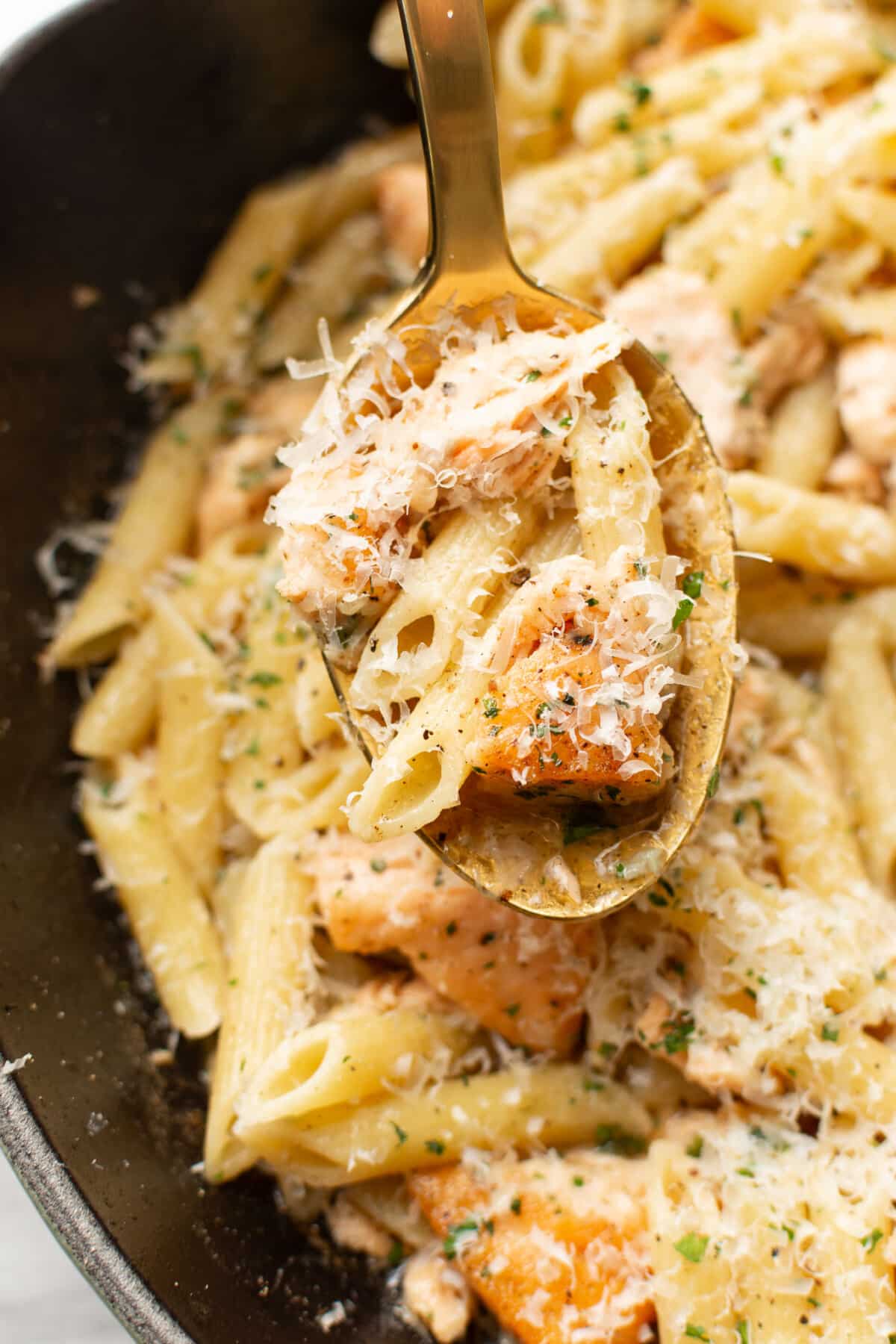 a skillet with garlic butter salmon pasta and a serving spoon