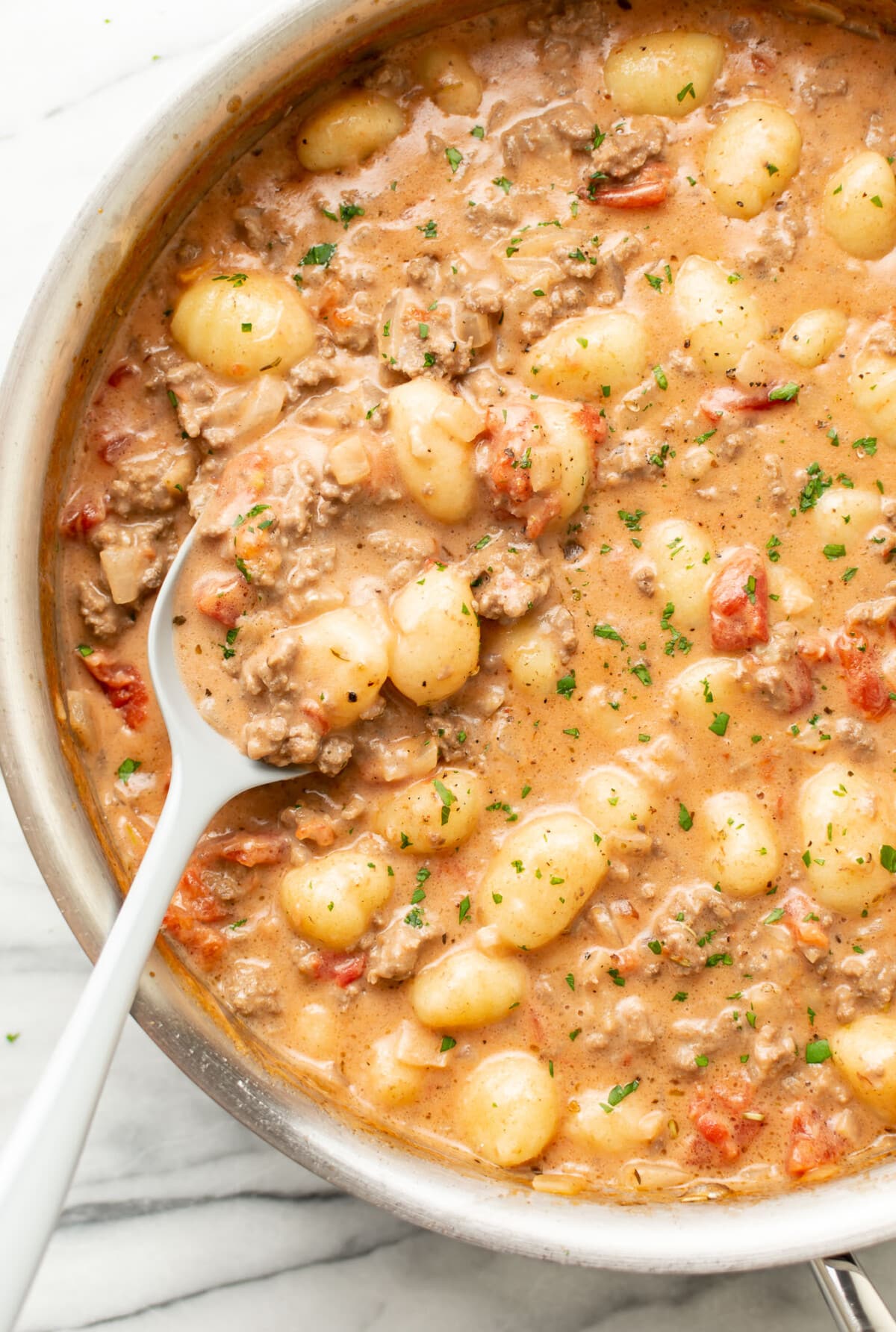 a pan with ground beef gnocchi and a serving spoon
