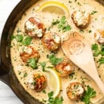 a skillet with creamy garlic lemon pan seared scallops and a wooden spoon