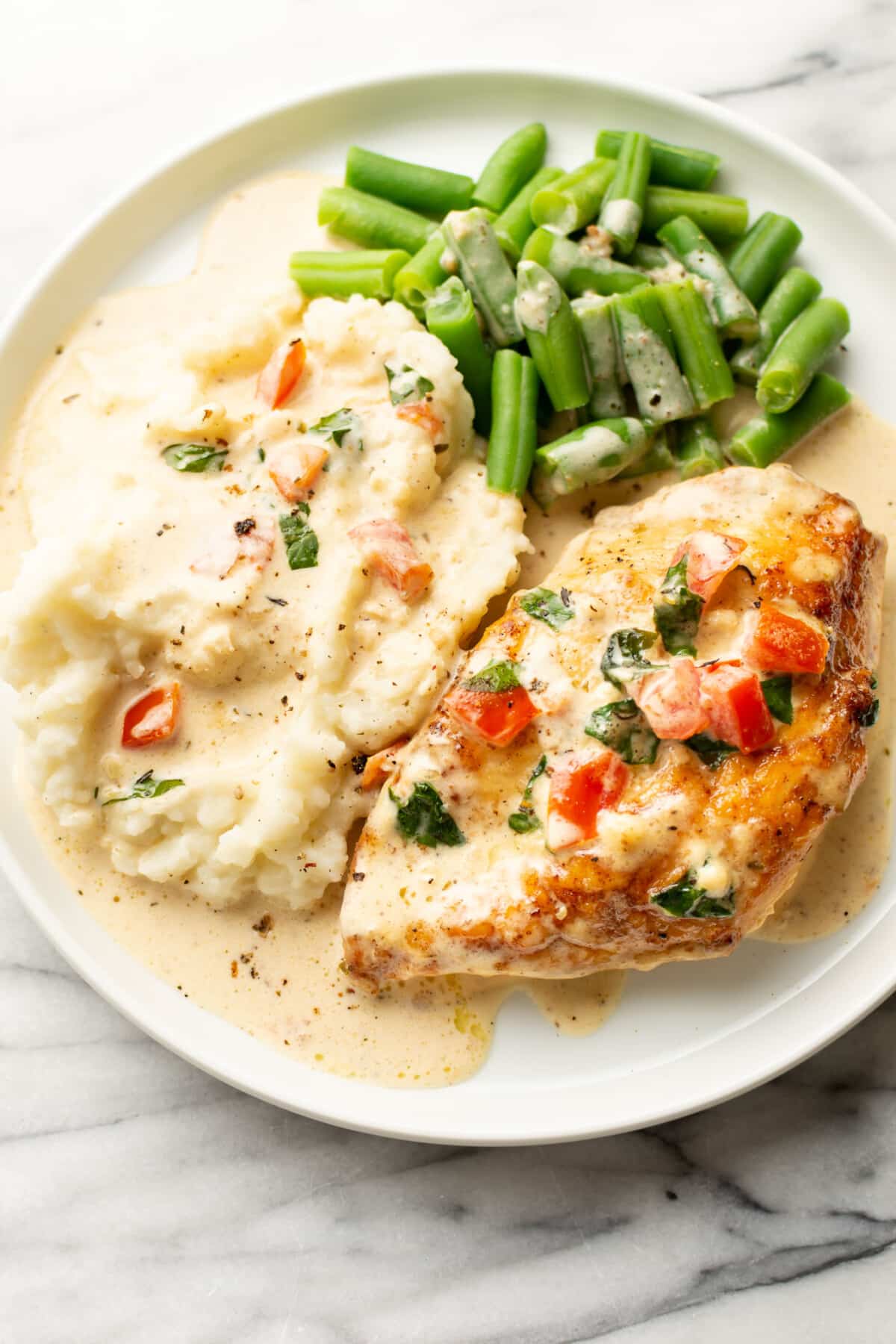 a plate with tomato basil chicken, mashed potatoes, and green beans