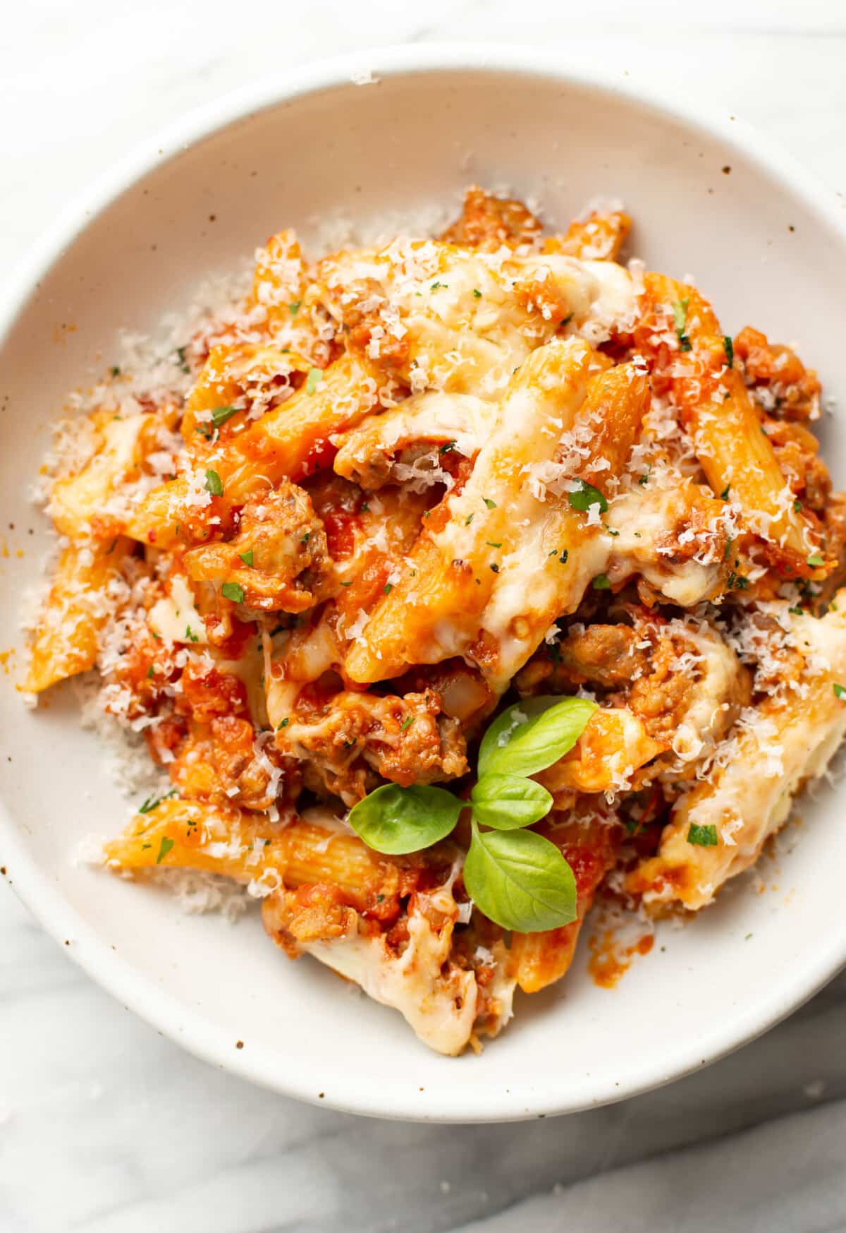a bowl with a portion of sausage penne bake and basil