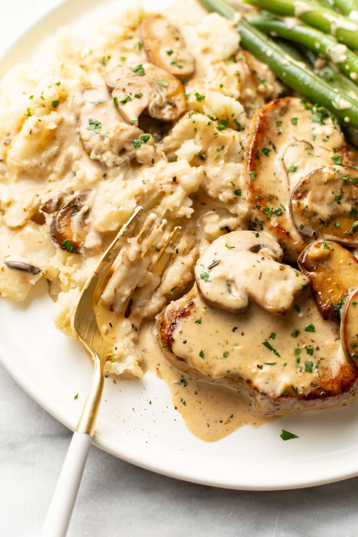 a plate with cream mushroom pork tenderloin, mashed potatoes, and green beans