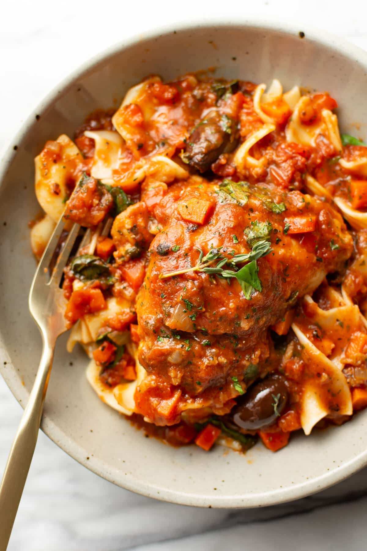 a bowl of chicken cacciatore over egg noodles with a fork