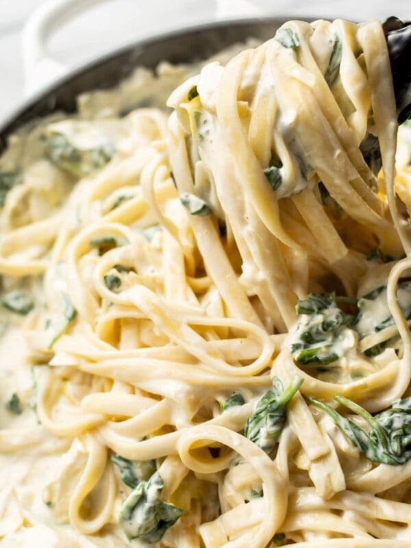 close-up of creamy spinach artichoke pasta being lifted up with tongs