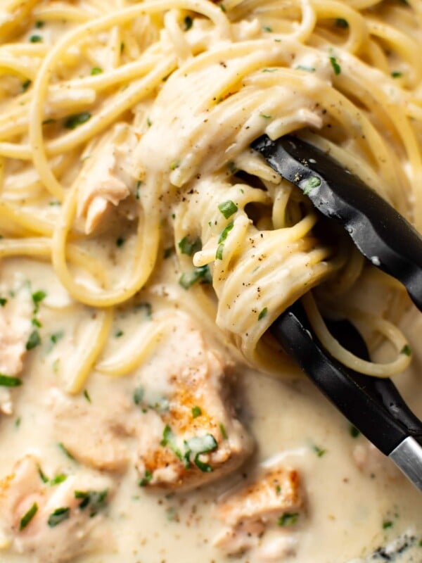 extreme close-up of serving tongs twirling creamy salmon spaghetti