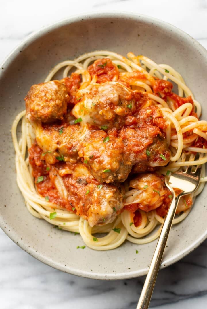 cheesy baked meatballs on a bed of spaghetti with a fork