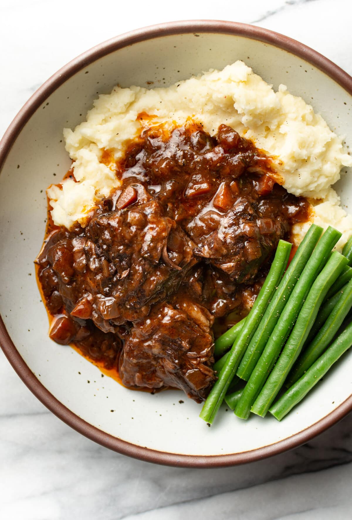 a bowl with red wine braised short ribs, mashed potatoes, and green beans