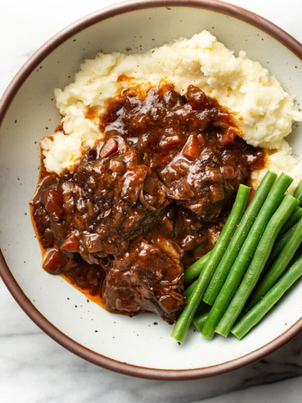 a bowl with red wine braised short ribs, mashed potatoes, and green beans