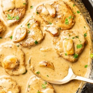 a skillet with creamy garlic pork tenderloin and a serving spoon