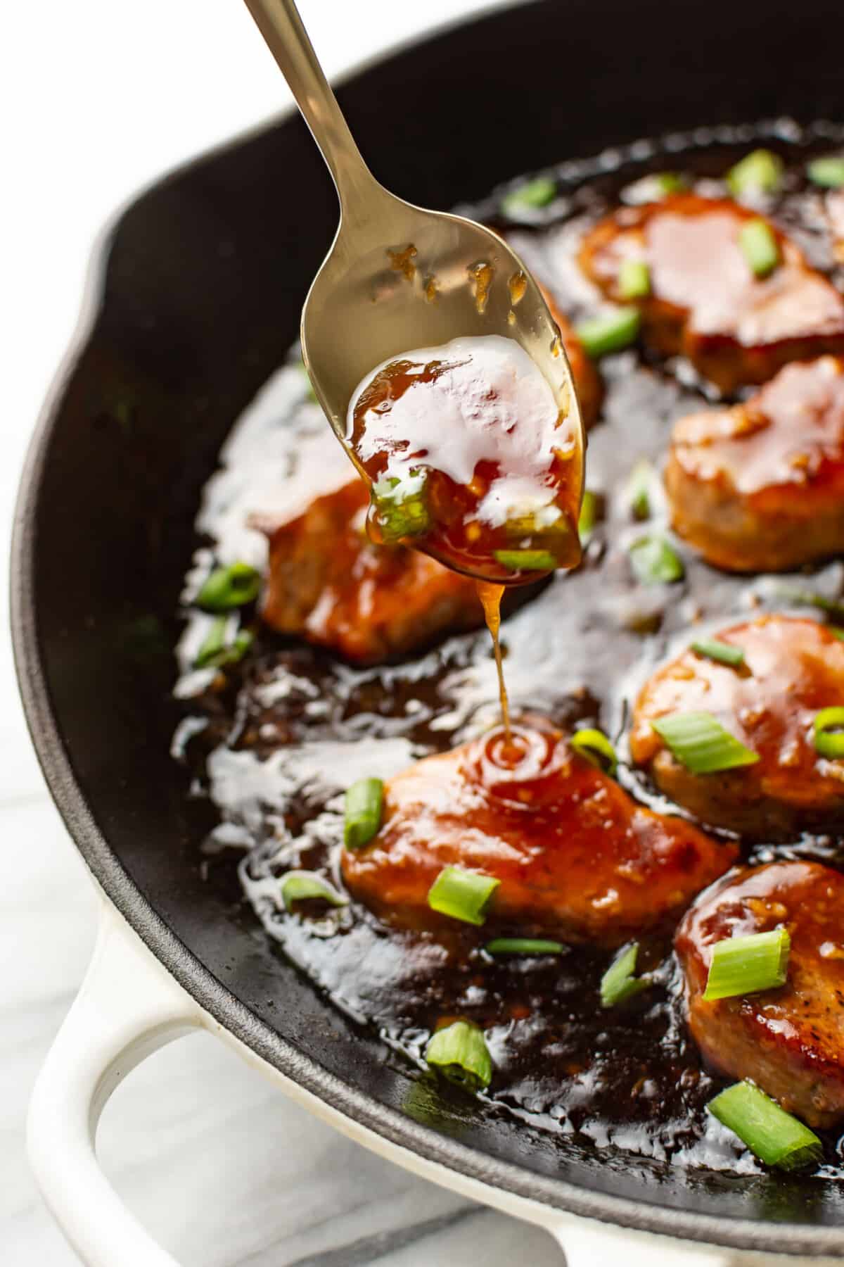 a skillet with honey garlic pork tenderloin and a serving spoon
