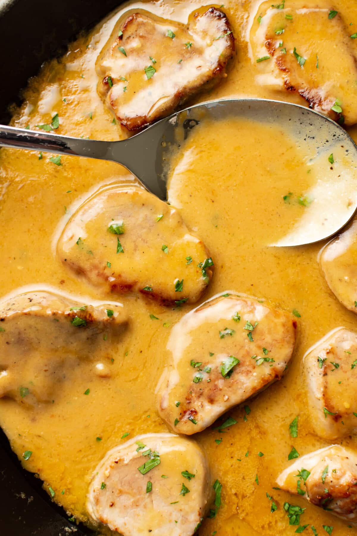 closeup of a skillet with honey mustard pork tenderloin and a serving spoon
