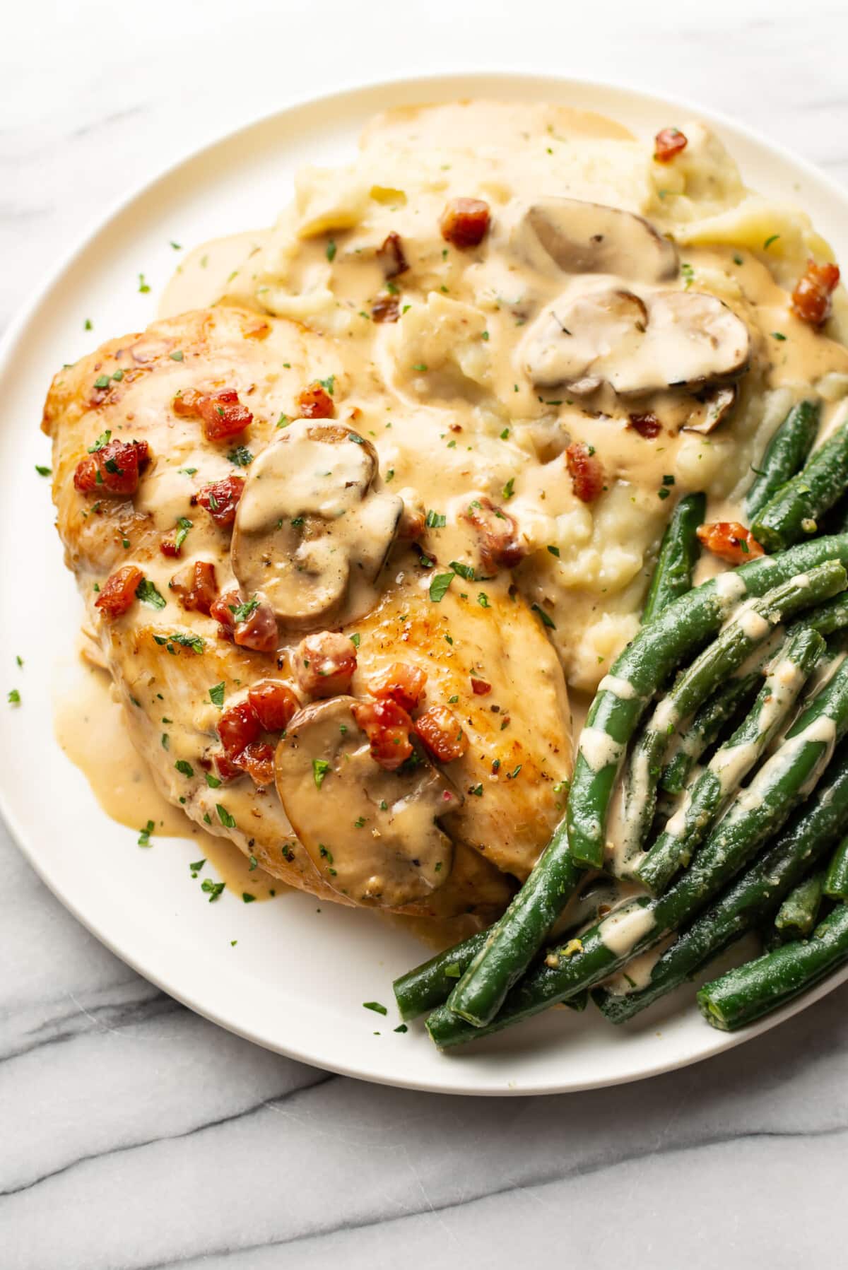 a plate with pancetta mushroom chicken, mashed potatoes, and green beans