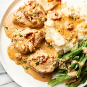 a plate with marry me pork tenderloin, mashed potatoes, and green beans