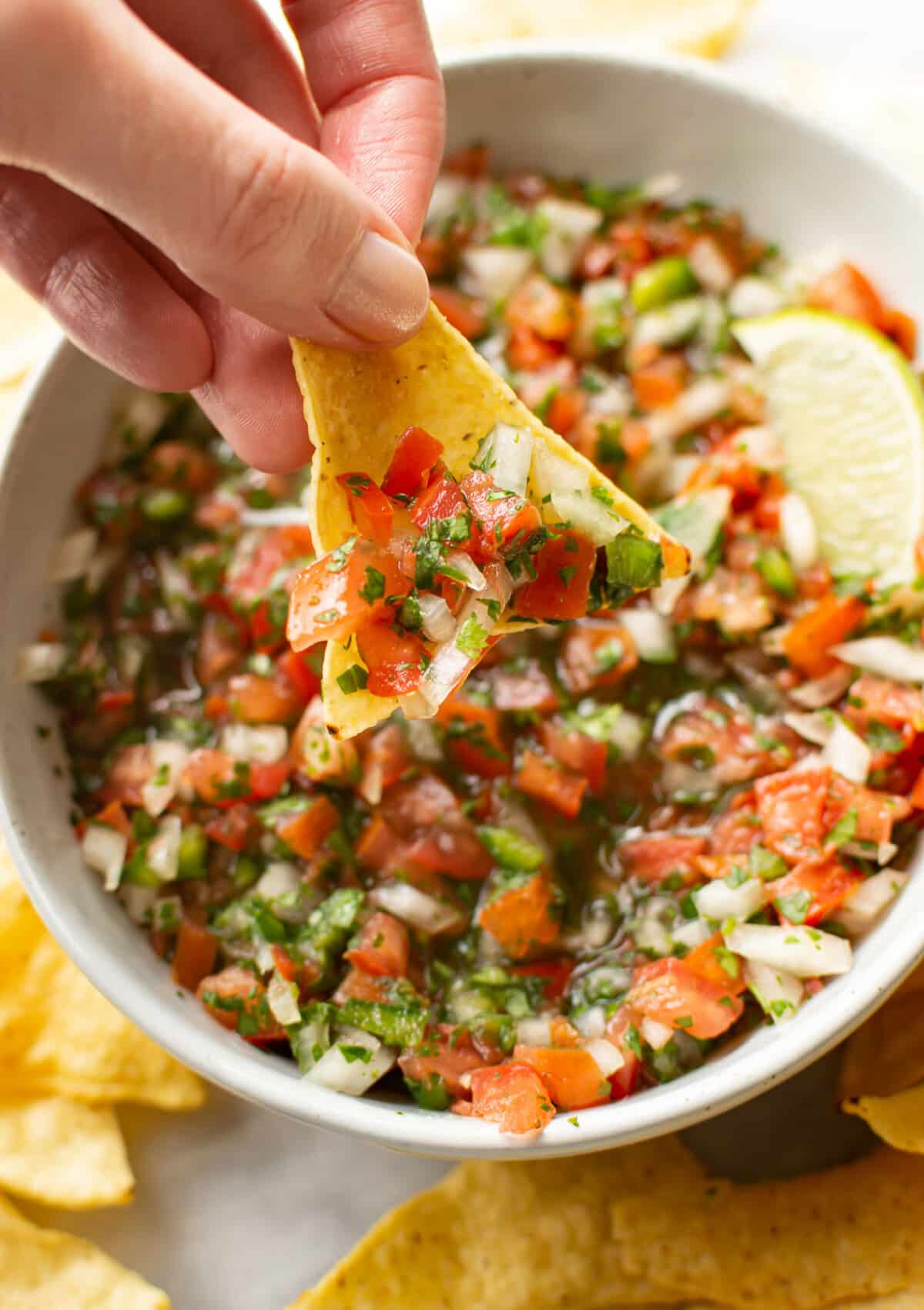 a female hand dipping a tortilla chip into pico de gallo