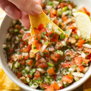 a female hand dipping a tortilla chip into pico de gallo
