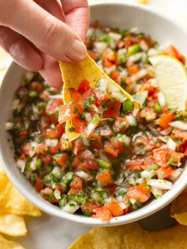 a female hand dipping a tortilla chip into pico de gallo