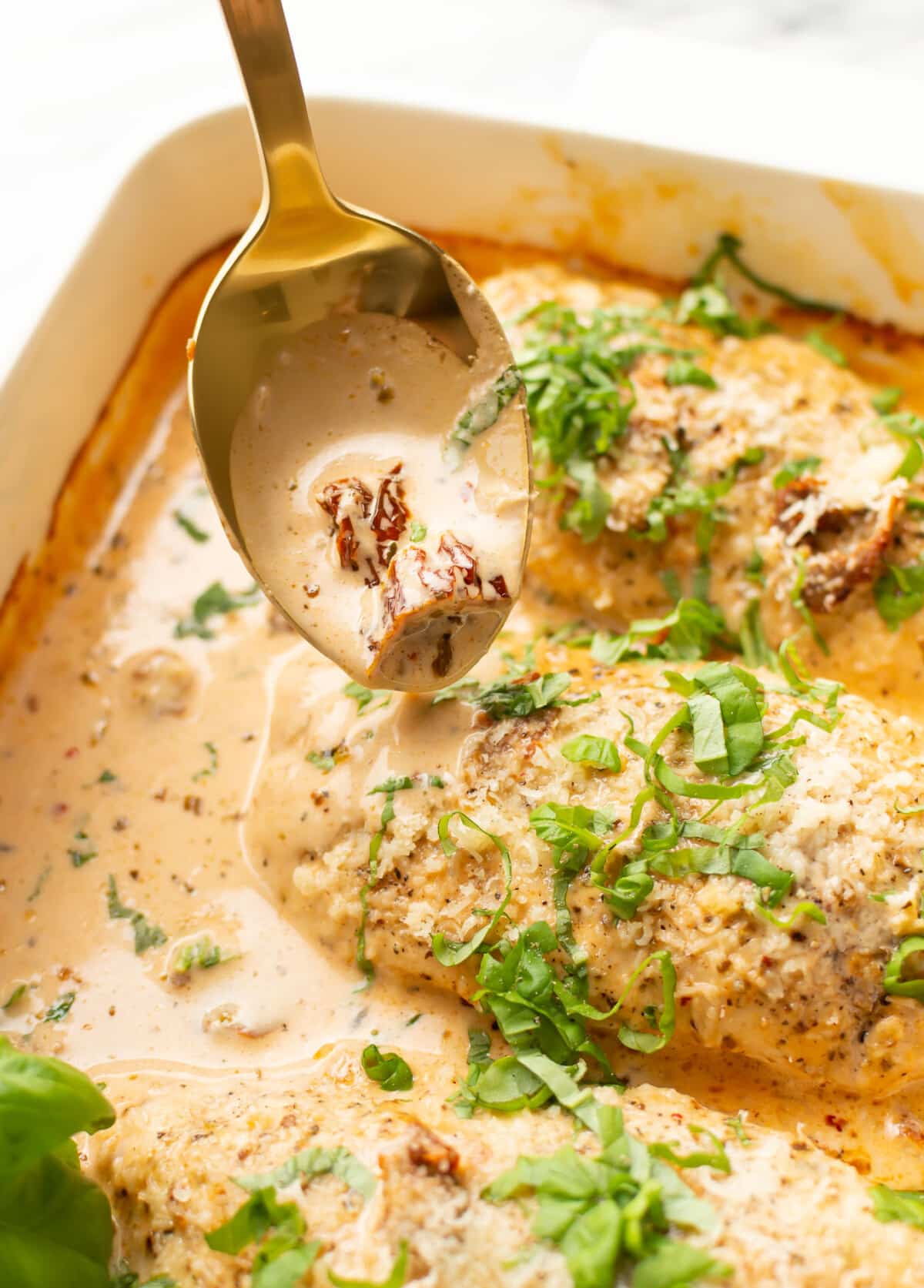 a baking dish with baked marry me chicken breasts and a serving spoon