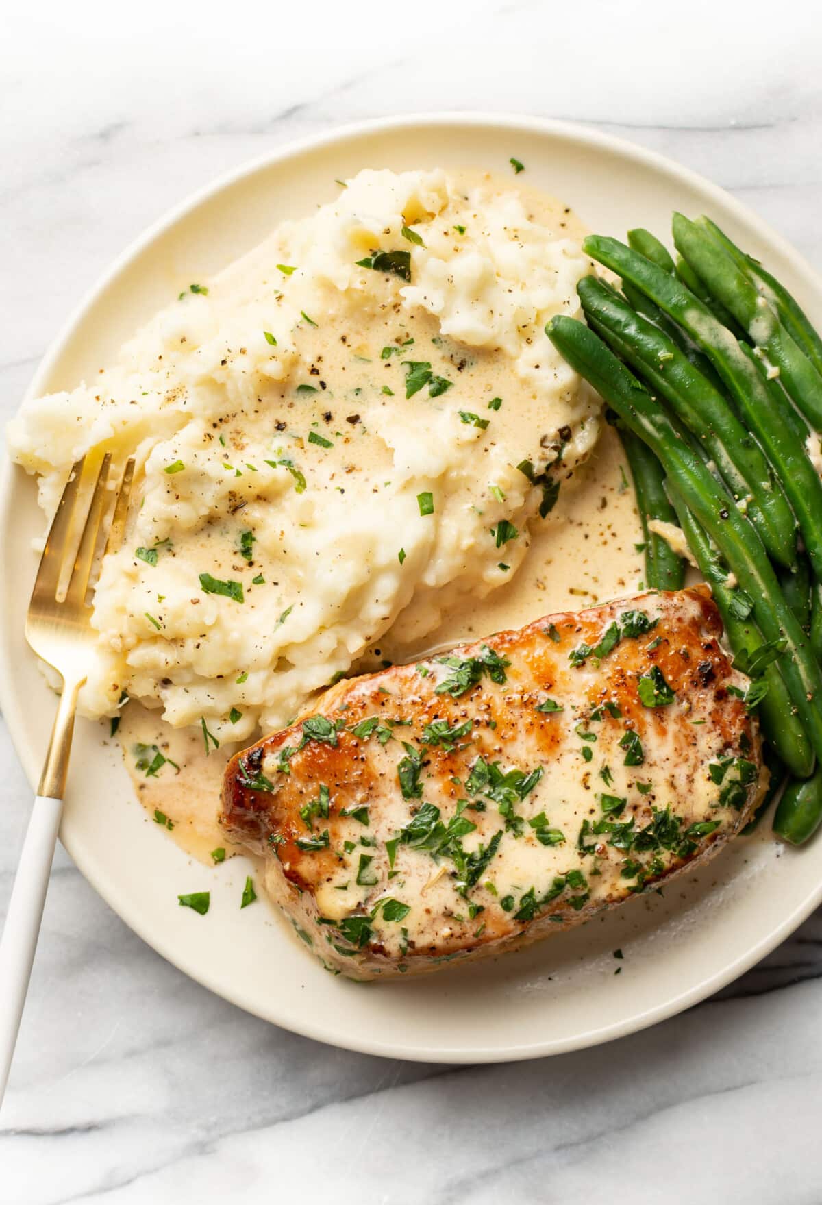 a plate with creamy white wine pork chops, green beans, and mashed potatoes with a fork