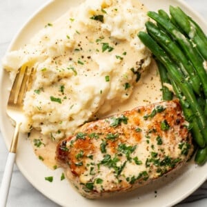a plate with creamy white wine pork chops, green beans, and mashed potatoes with a fork