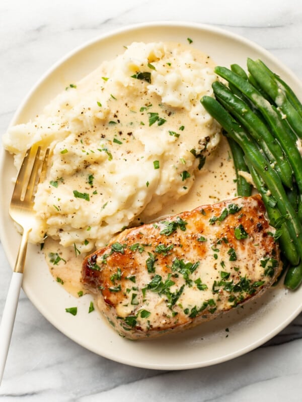 a plate with creamy white wine pork chops, green beans, and mashed potatoes with a fork