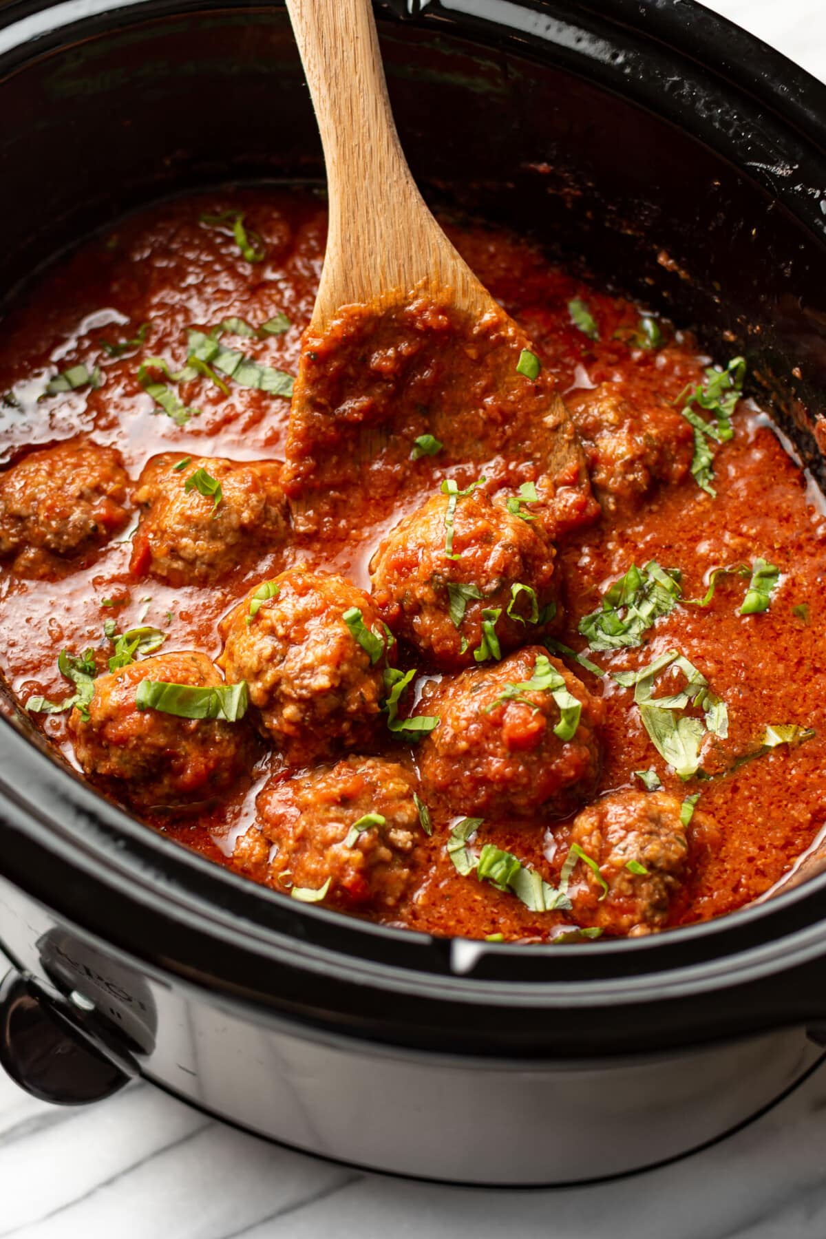 a crockpot with meatballs in tomato sauce with a wooden spoon