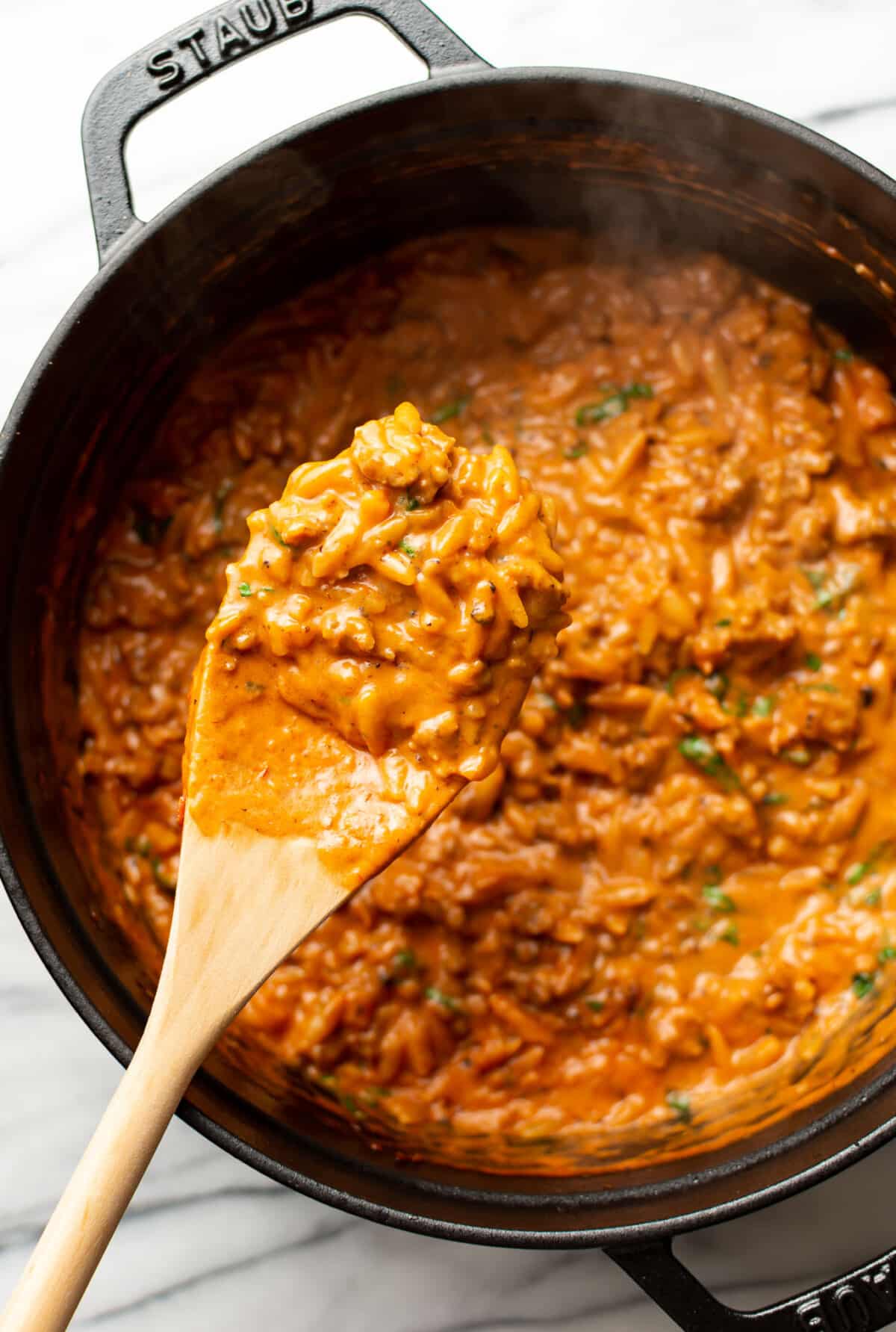 a pot of spicy italian sausage orzo with a wooden spoon