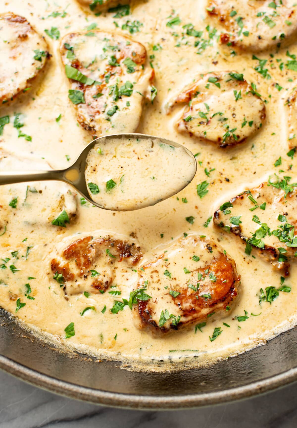 spooning sauce over a skillet with creamy white wine pork tenderloin