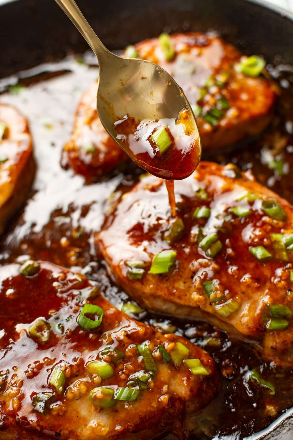 spooning honey garlic sauce over pork chops in a skillet