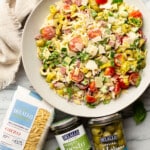 a bowl of italian orzo salad next to olives and other ingredients