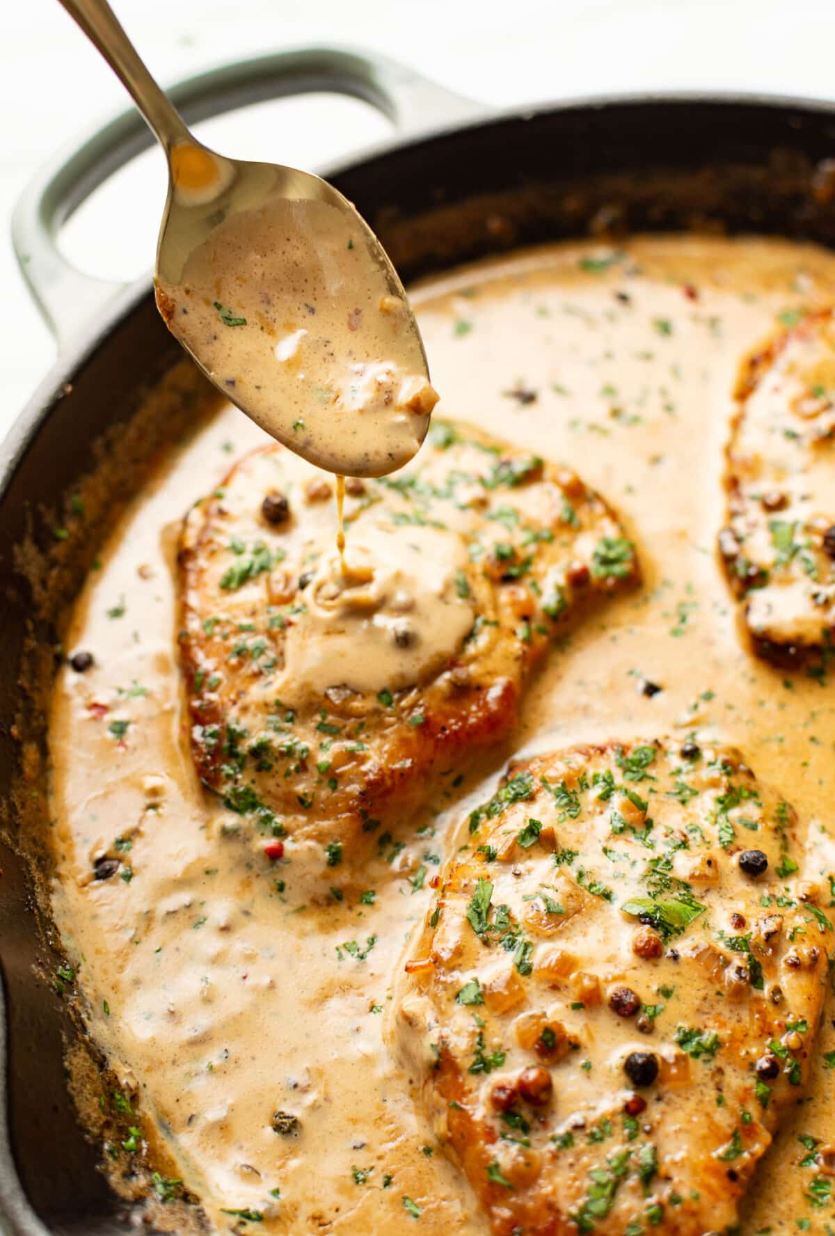 spooning peppercorn brandy sauce over a skillet with pork chops