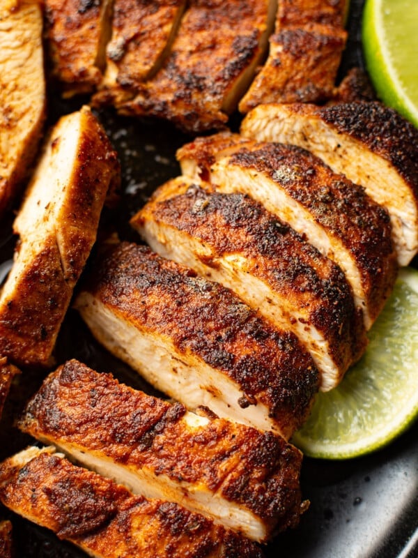 sliced blackened chicken on a plate next to lime wedges