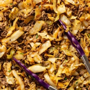 a skillet with ground beef and cabbage with kitchen tongs