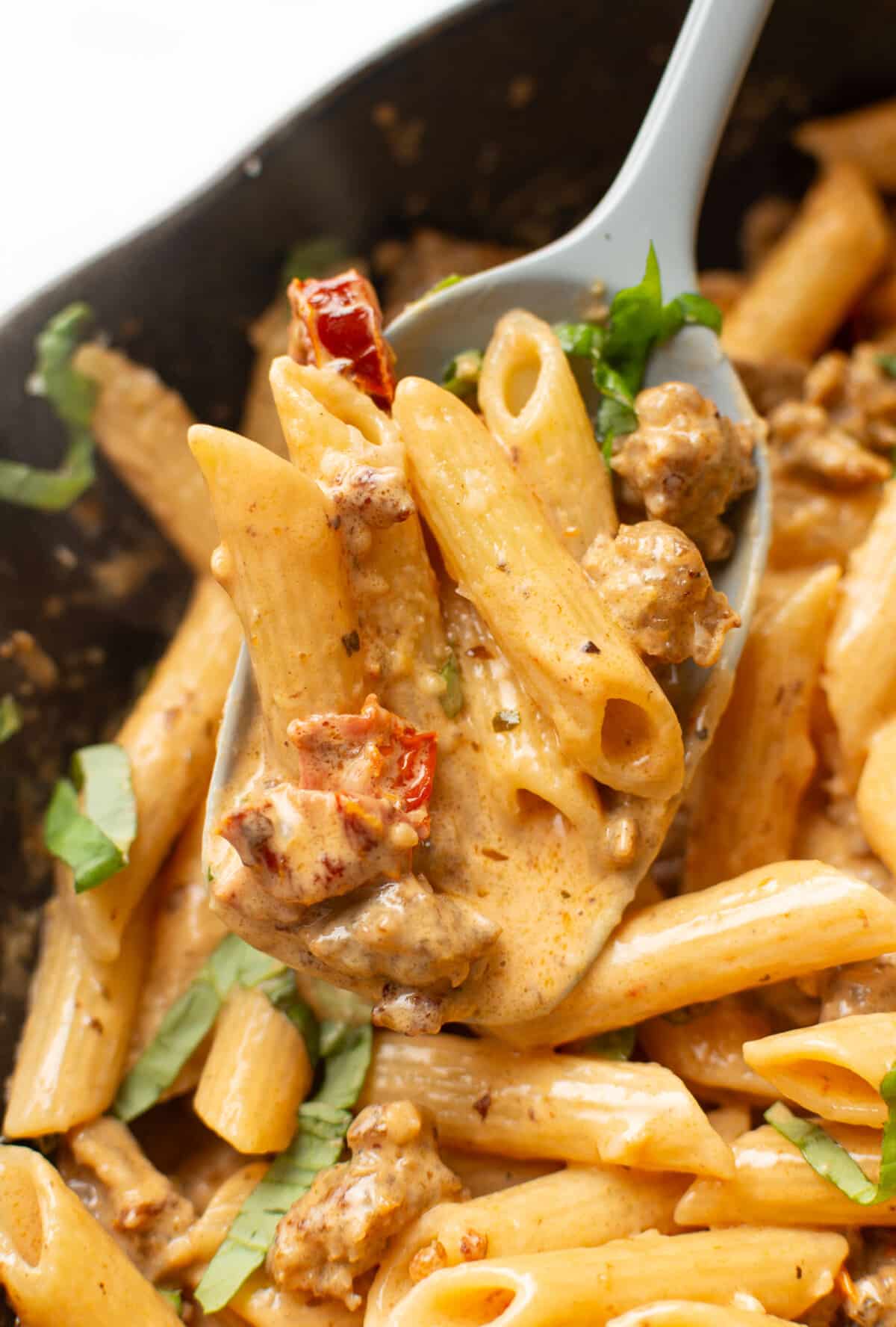 a skillet with marry me sausage pasta and a serving spoon