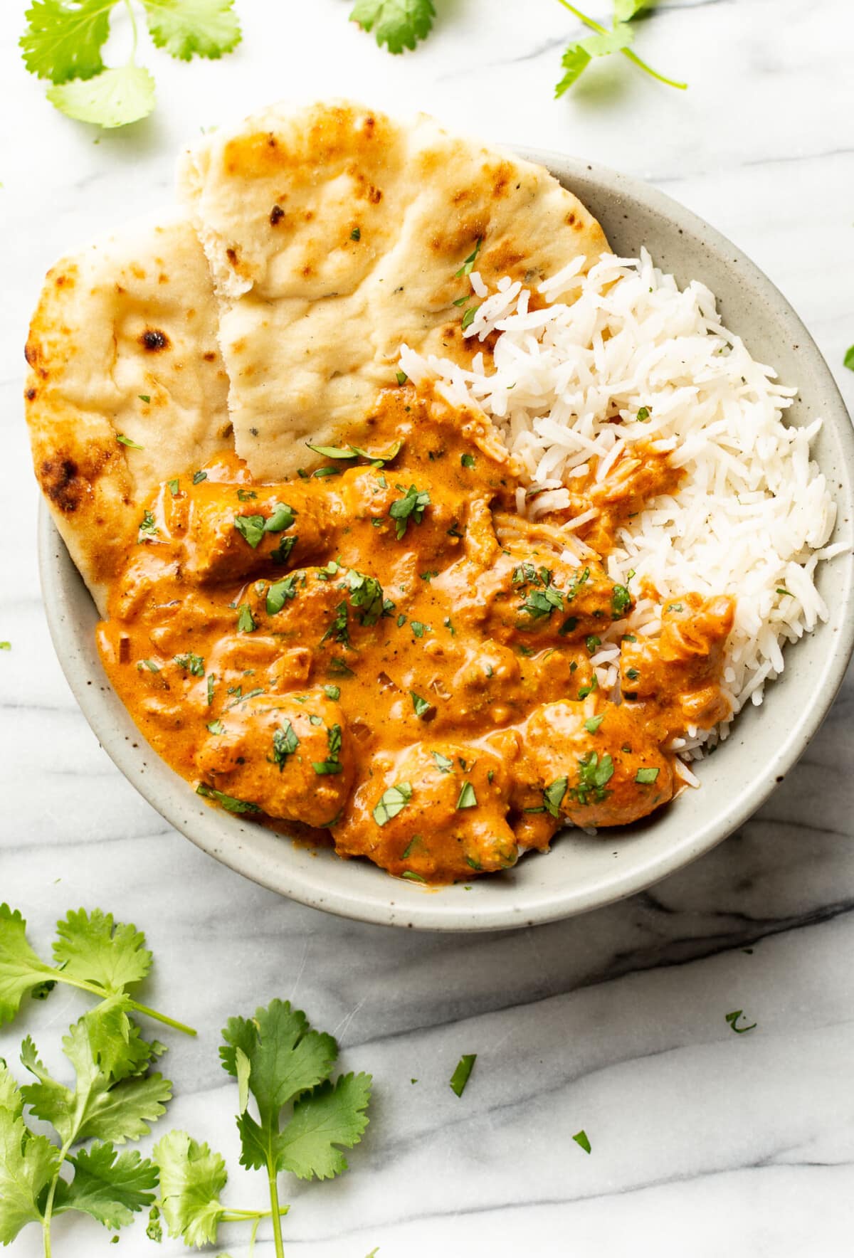 a bowl of butter chicken with basmati rice and naan