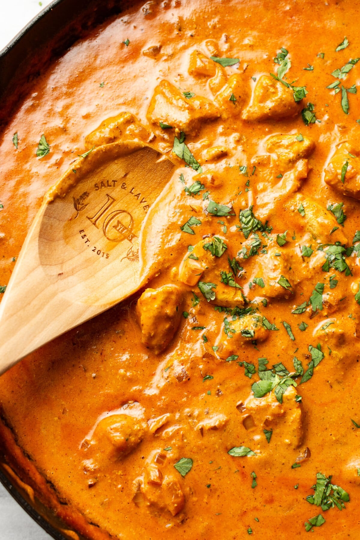a skillet with homemade butter chicken and a wooden serving spoon