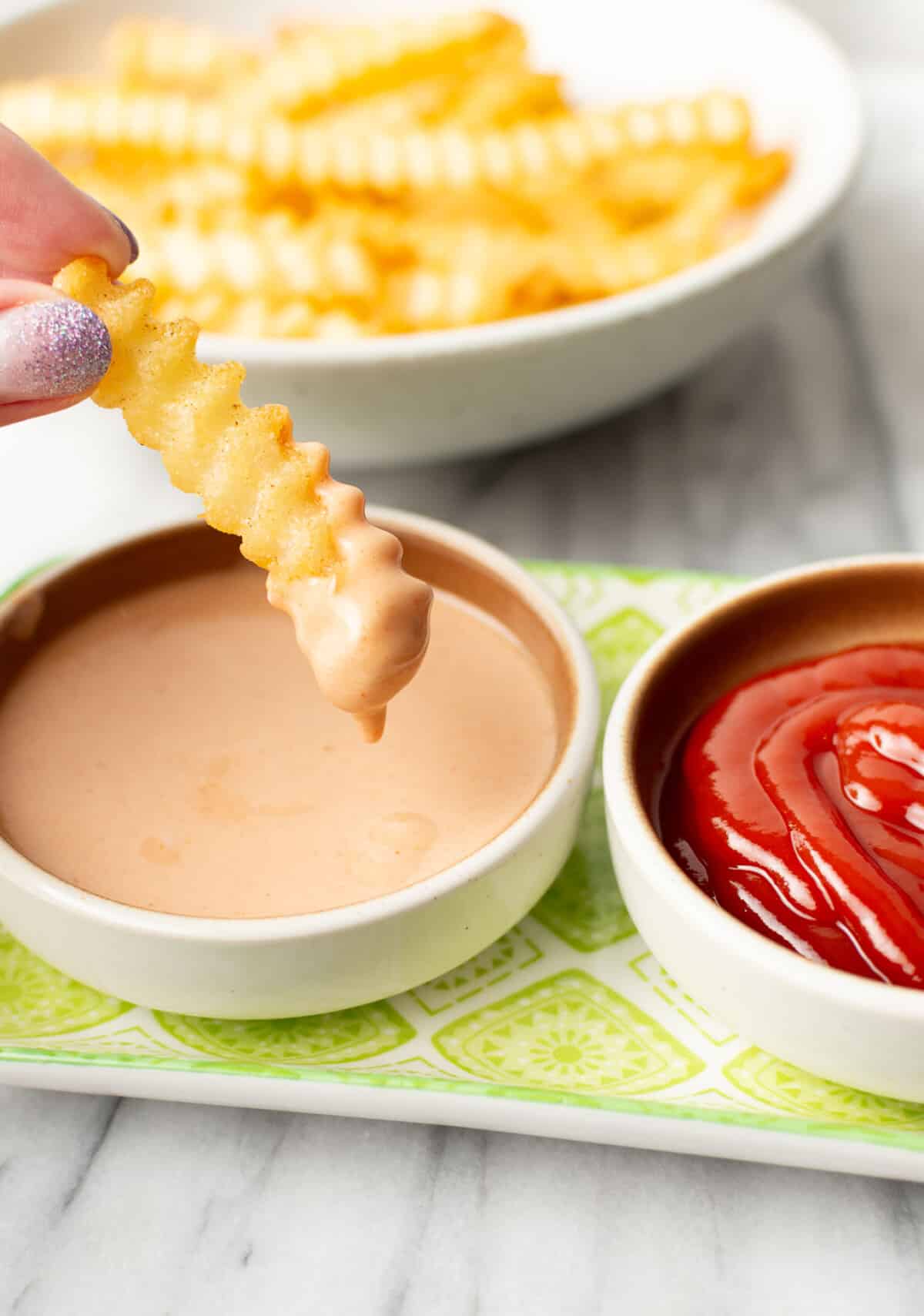 a female hand dipping a french fry into homemade fry sauce