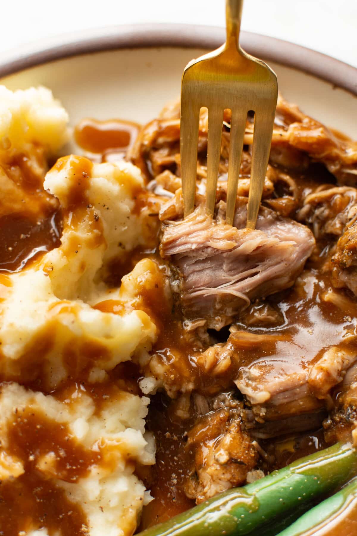 closeup of a plate with pork roast, mashed potatoes, gravy, and green beans with a fork