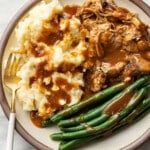 a plate with pork roast, green beans, mashed potatoes, gravy, and a fork