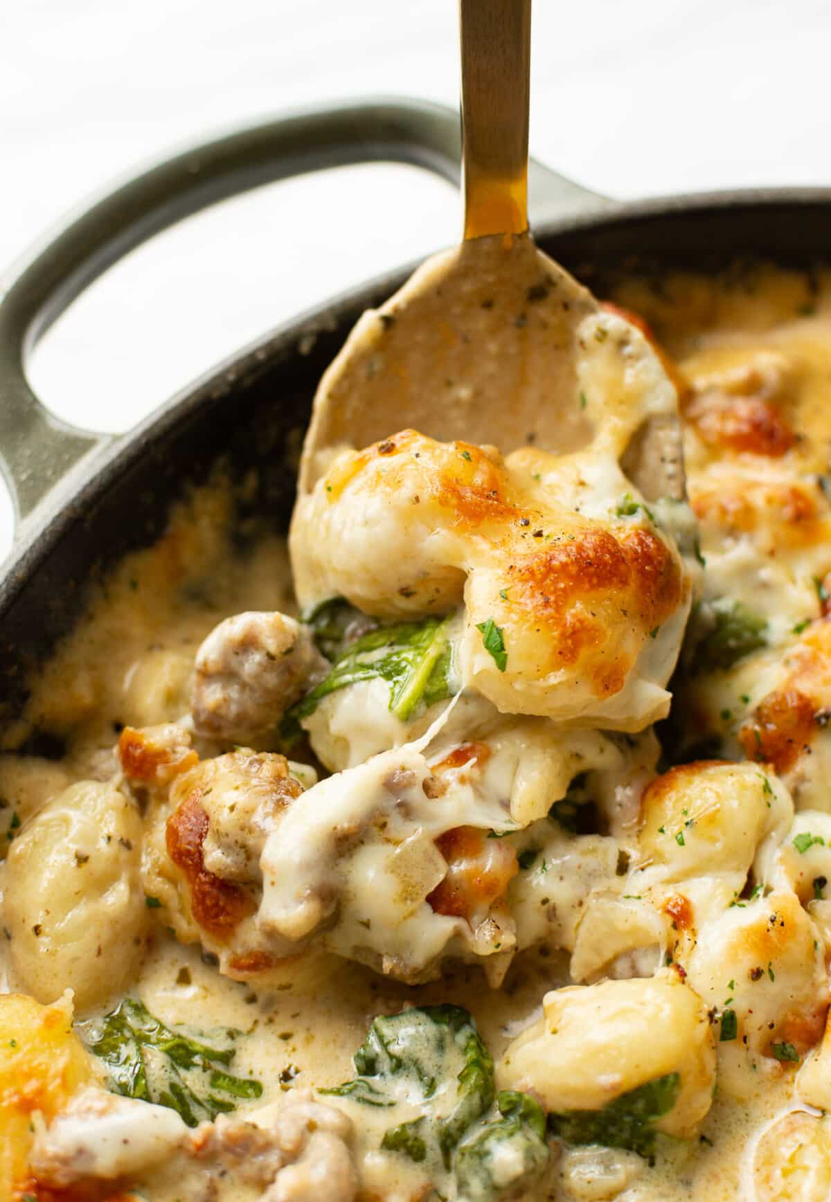 closeup of a skillet with pesto sausage gnocchi bake and a serving spoon
