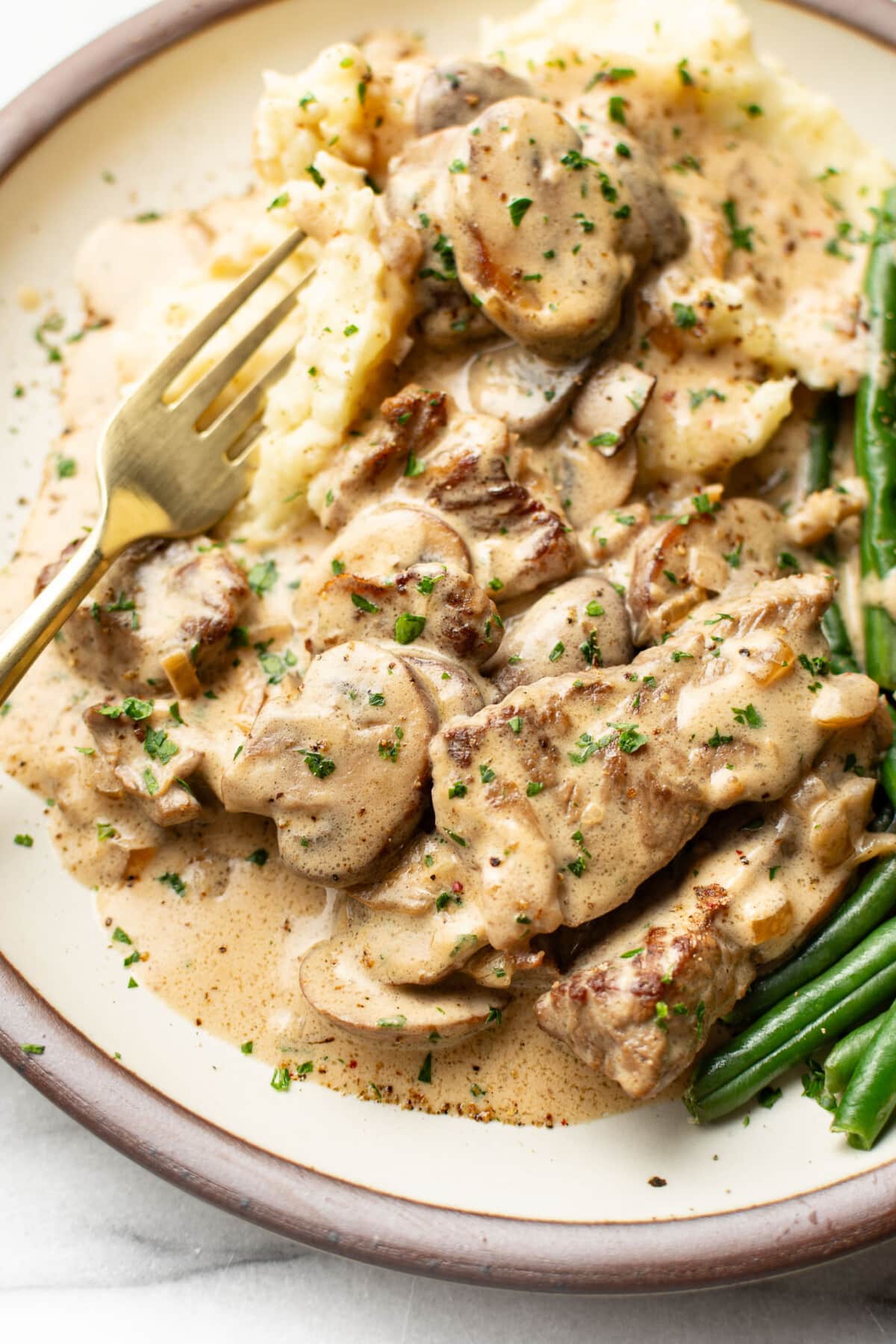 a plate with beef stroganoff, mashed potatoes, and green beans