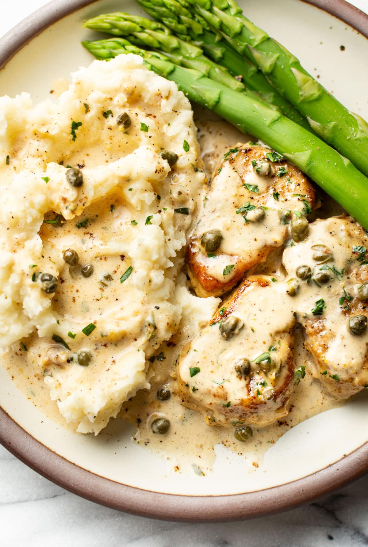 a plate with pork tenderloin piccata, asparagus, and mashed potatoes